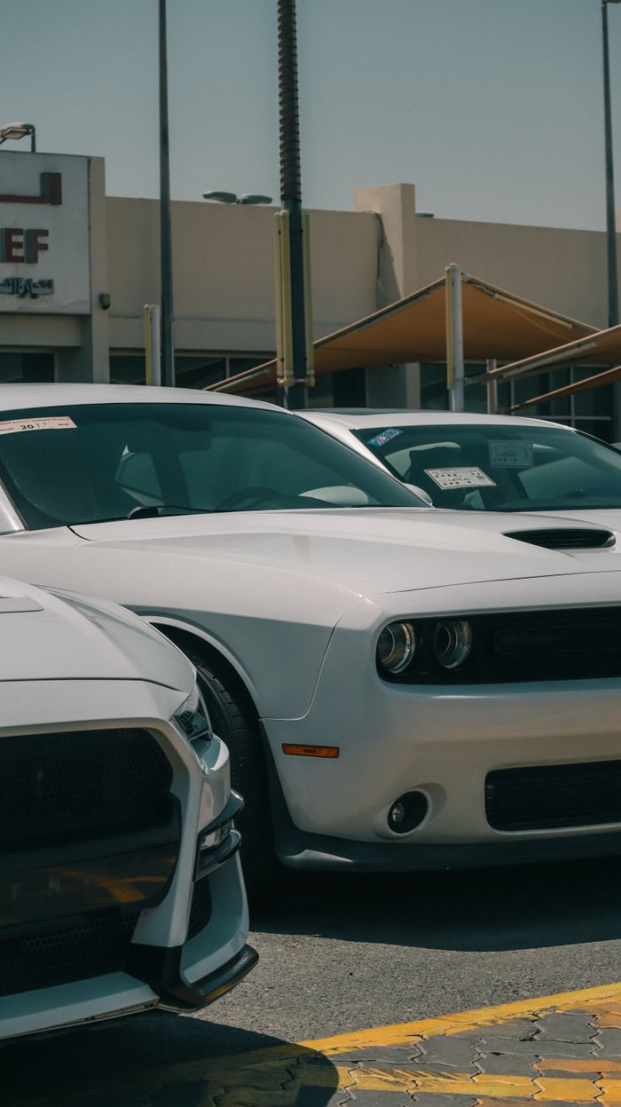 White Dodge Challenger in a car dealership parking lot during the day.